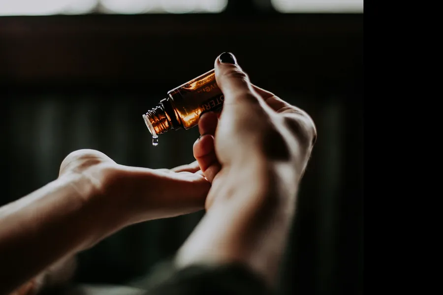 A drop of oil falls from a dropper into the palm of a hand